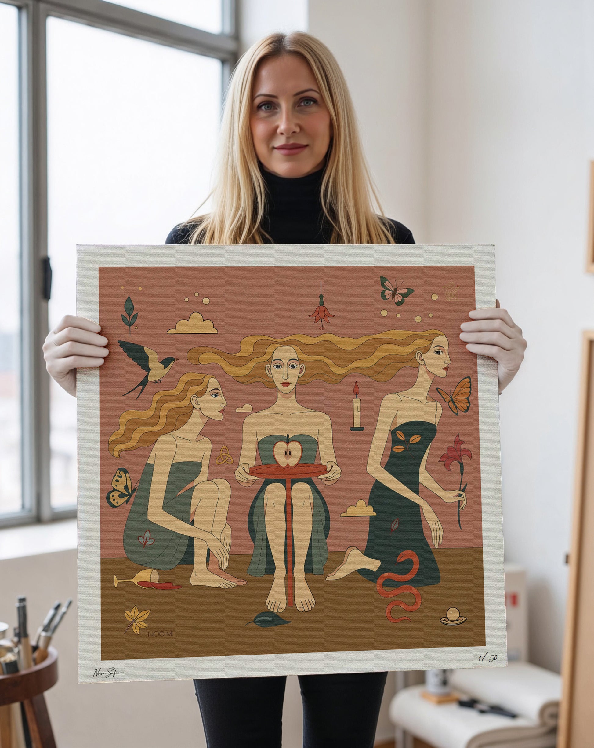 Woman holding A Limited Edition NOE MI wall art print of three women with various symbols