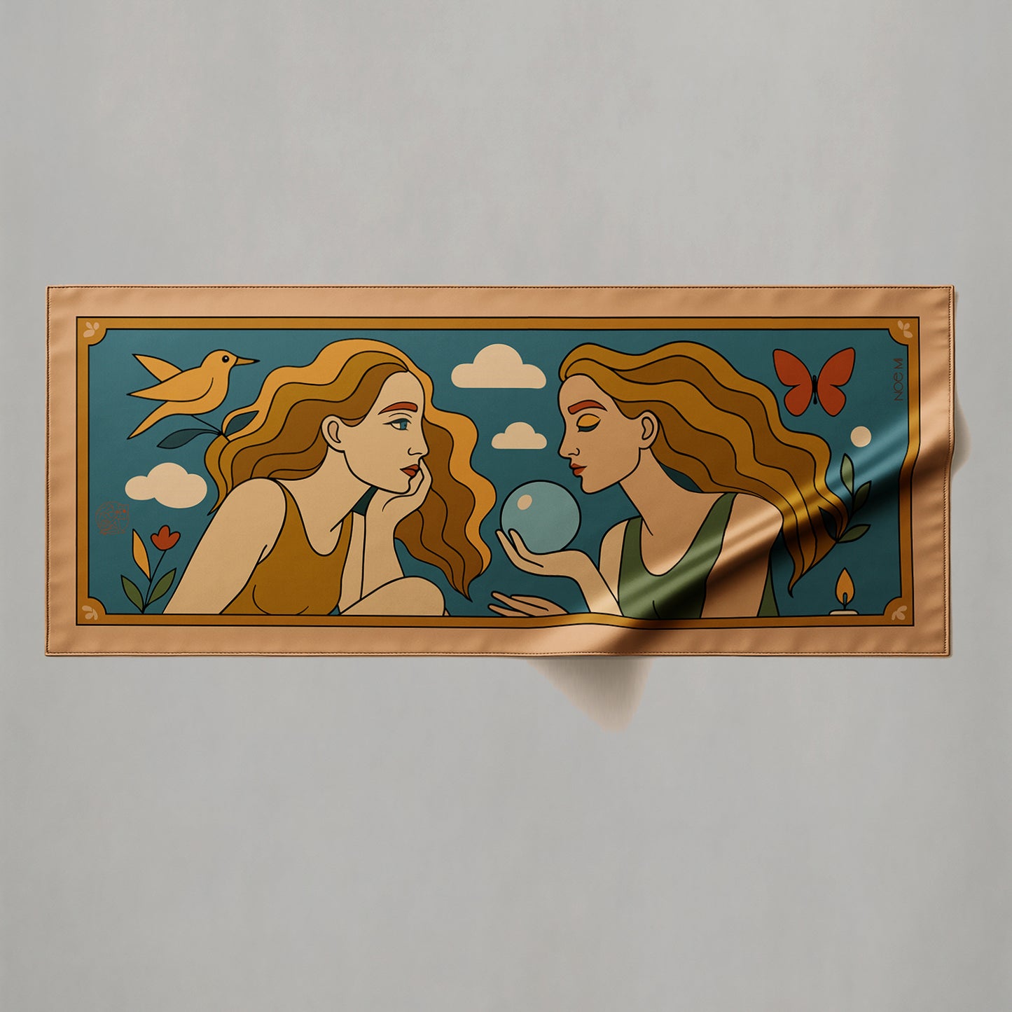 a colorful silk or chiffon pareo/sarong of two women with long hair, one holding a blue orb, on a fabric background.