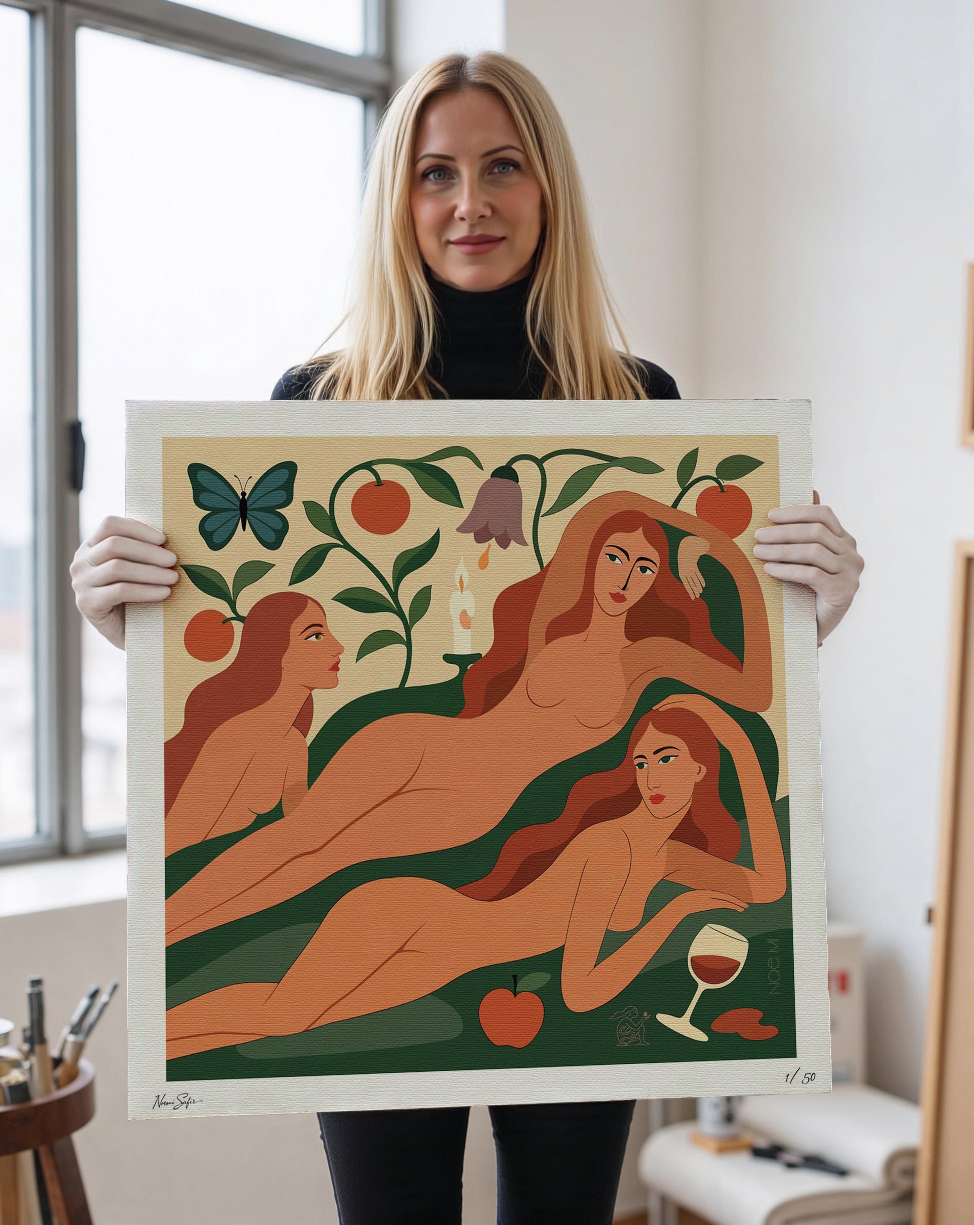 Woman holding a framed  Limited Edition NOE MI wall art print of three women with nature elements.