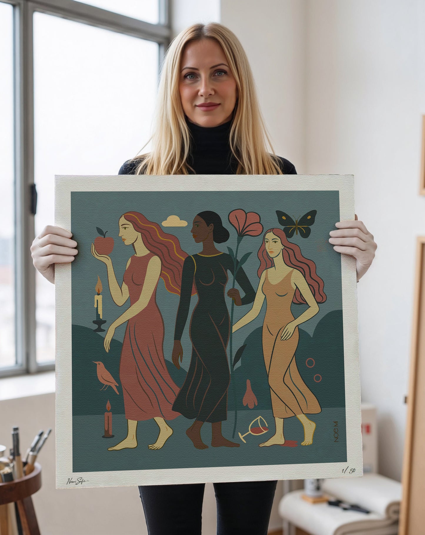Woman holding a Limited Edition NOE MI wall art print of three women with different skin tones.