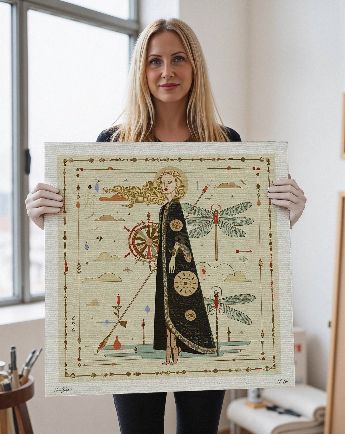 Noemi Safir holding one of her limited edition prints featuring a decorative design showing a central woman figure, symbols and graphical elements. NOE MI