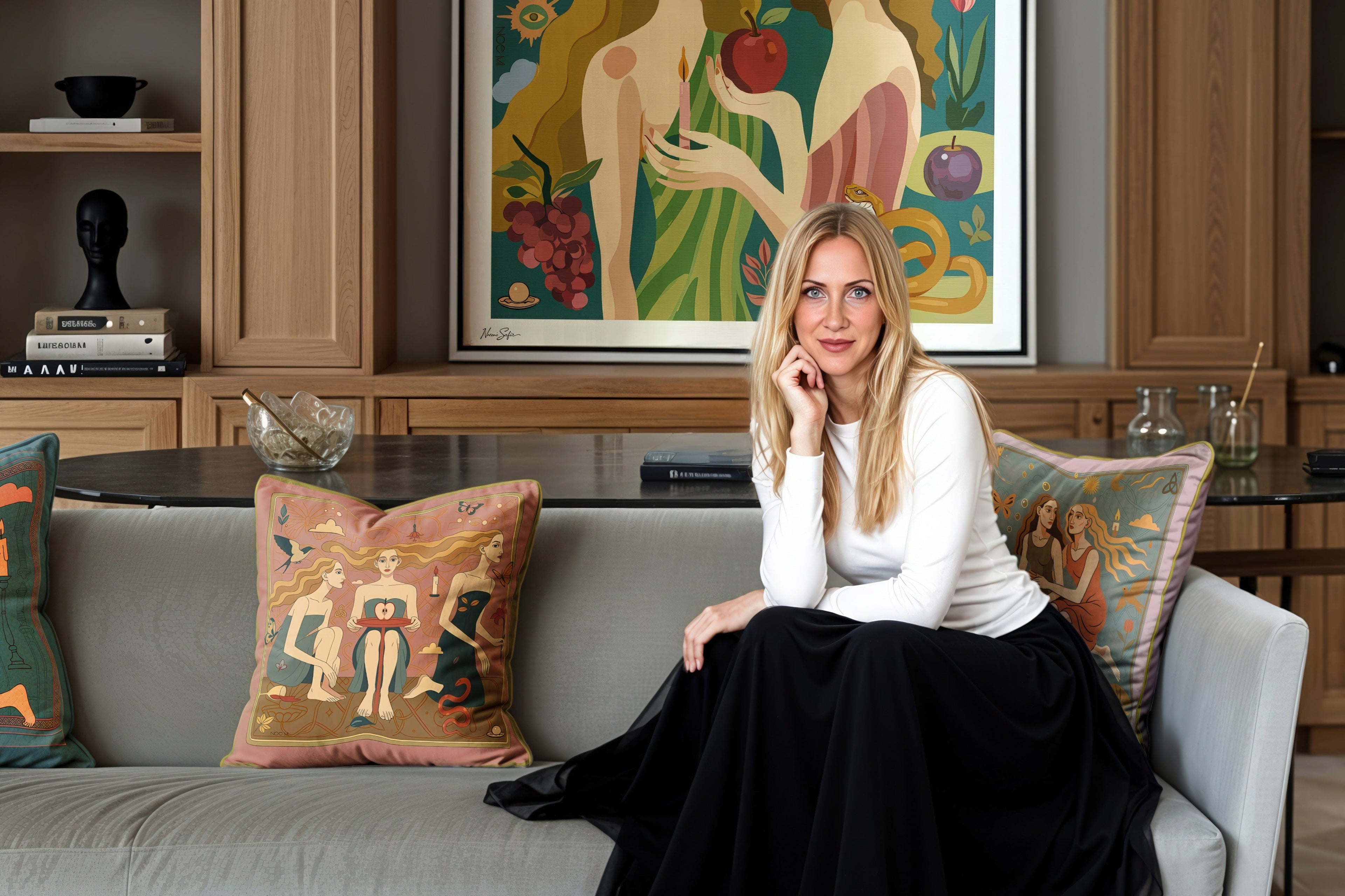 Noemi Safir sitting on a couch in a stylish living room with a large NOE MI PRINT of two women holding an apple.