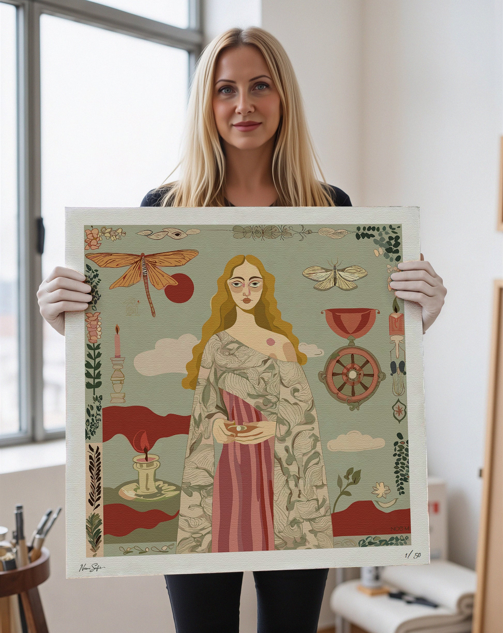 Noemi Safir holding a framed artwork print with a colorful design of a woman, dragonfly, and other elements.