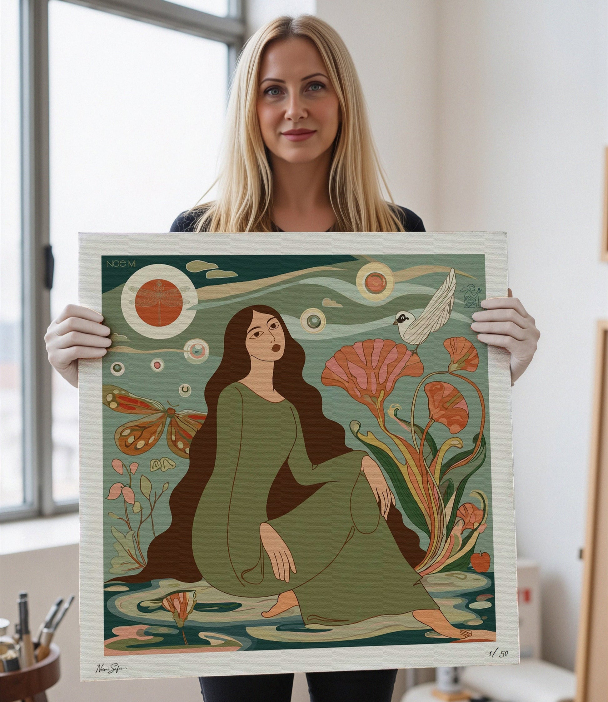 Noemi Safir artist holding a limited edition print of a woman sitting among flowers and nature elements. Vibrant, fade‑resistant inks for long‑lasting beauty by NOE MI